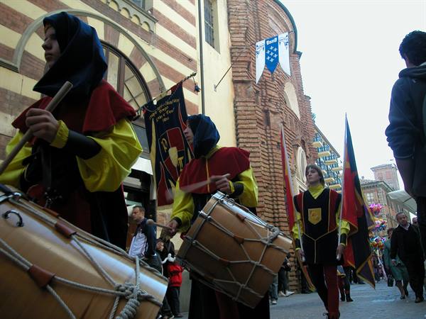 Drummers in medieval costumes parade with flags among brick buildings