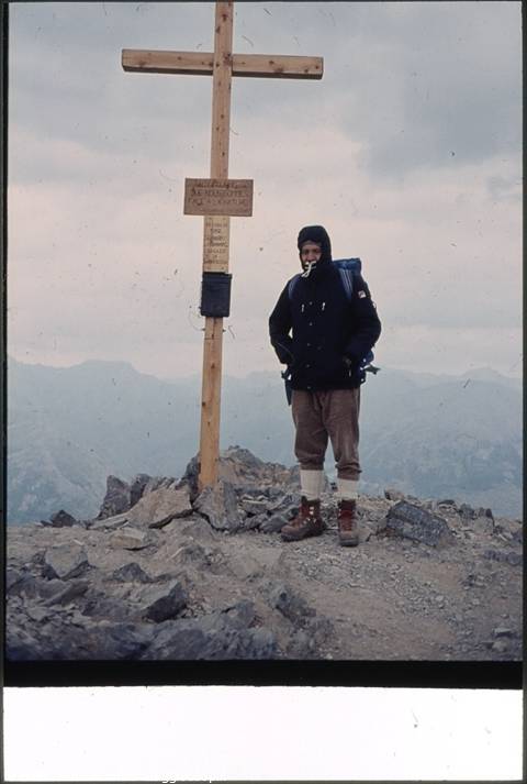 Hiker with backpack beside a wooden cross on a rocky summit