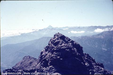 Rocky summit with snow-capped alpine peaks on the horizon above low clouds