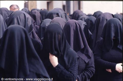 Women in black veils covering their faces, gathered in daylight procession