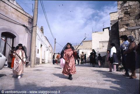 Children in satin robes carrying blades parade through the street