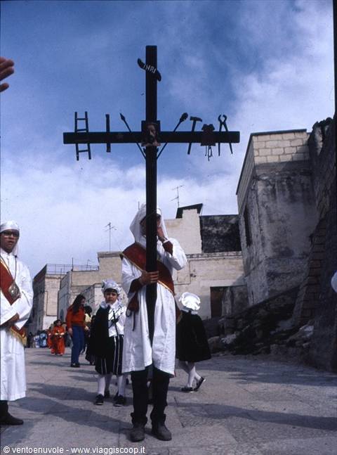 Procession in Matera: penitent in white carrying black cross among stone alleys