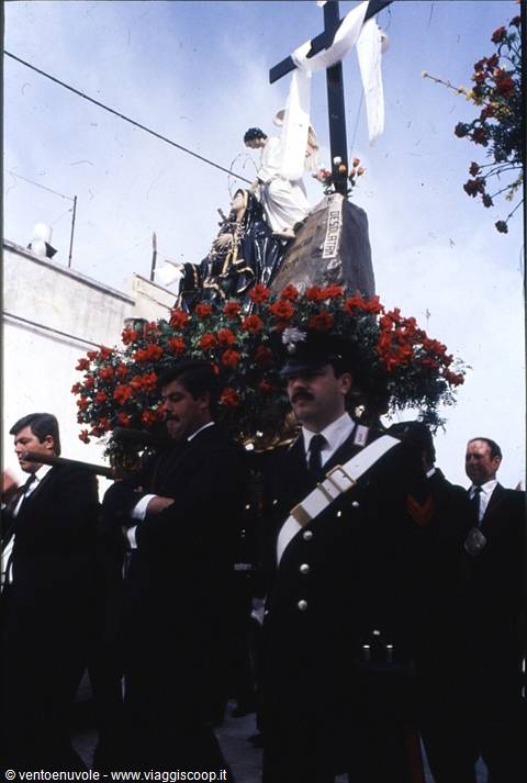 Procession with cross and statues among red flowers carried by men