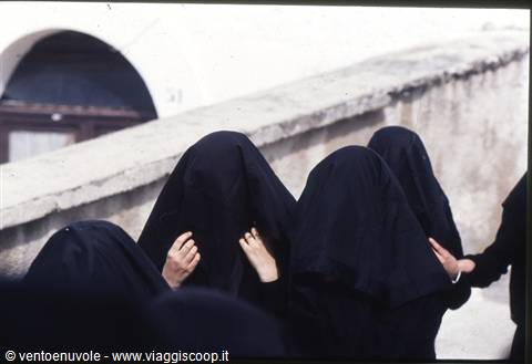 Women in black veils walk along a stone wall in Sarajevo