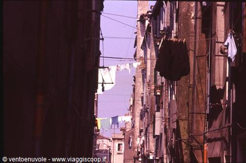 Laundry hanging between old stone houses in a narrow alley, harsh light