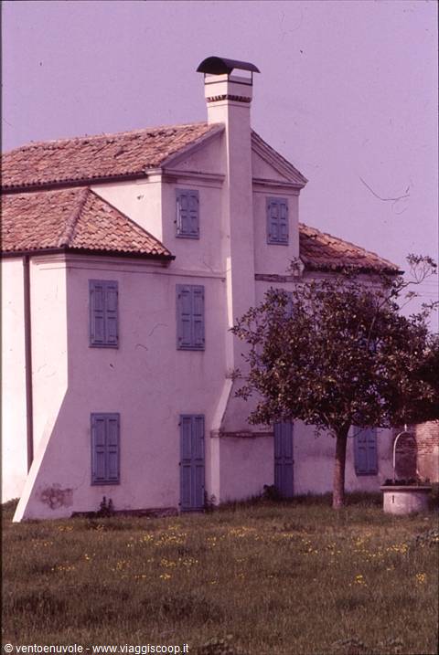 White farmhouse with terracotta roofs and chimney, flowery meadow in front
