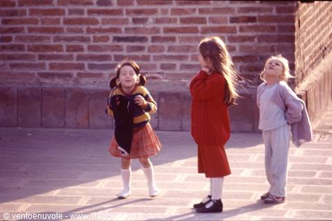 Three girls laughing in front of a red brick wall in sunlight
