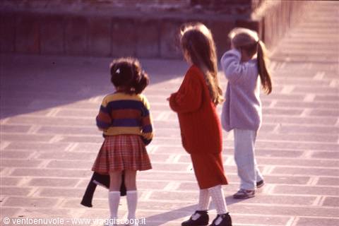 Three little girls in coats playing on a sunny paved square