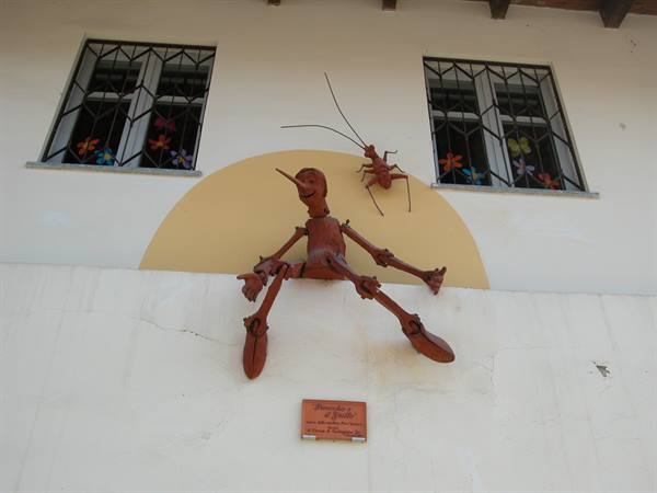 Metal sculpture of Pinocchio sitting with the Talking Cricket on a facade