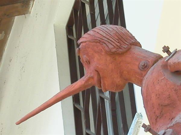 Terracotta Pinocchio statue with long nose in front of a metal grate