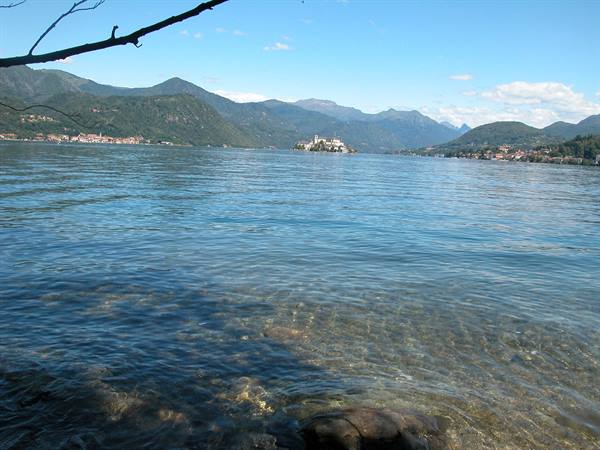 Isola San Giulio on Lake Orta, clear water, mountains and shadowed branches overhead