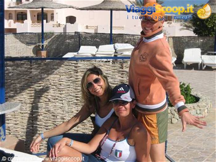 Three smiling tourists in caps beside straw umbrellas and white sun loungers