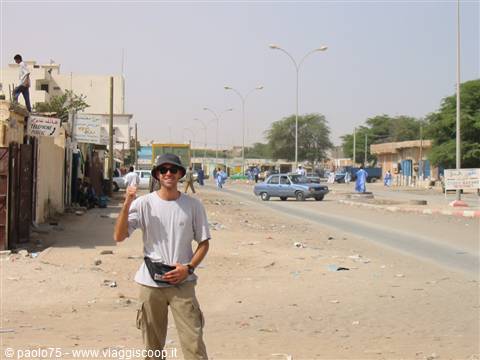 Hitchhiking tourist on sandy road, cars and men in blue robes