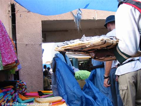 Man in blue robe carries a chair on shoulder through the market