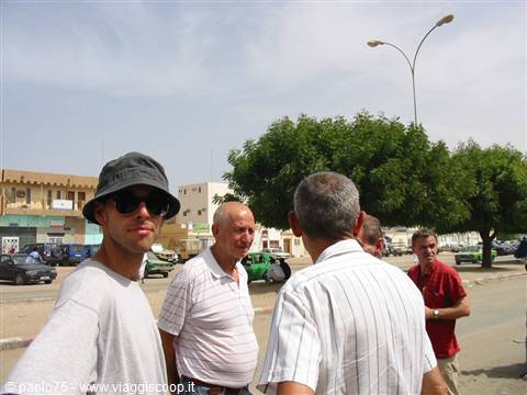 Group of tourists chatting along the road, green taxis and pale buildings behind