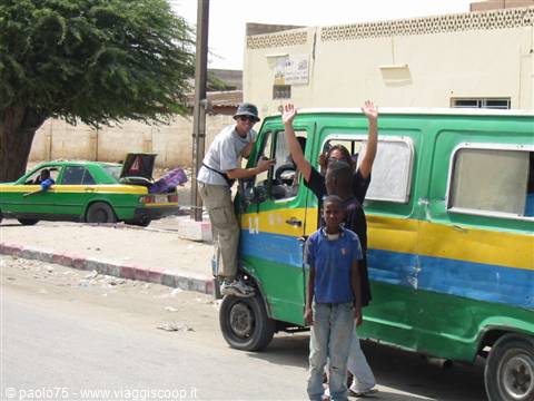 Tourists waving from a green and yellow minibus, taxi parked on the street