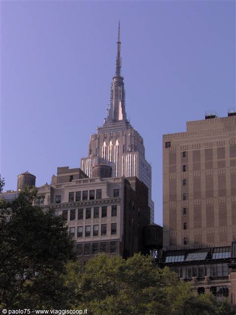The Empire State Building rising above brick buildings and green treetops