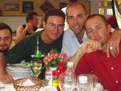 Four friends leaning on a restaurant table set with bottles and flowers