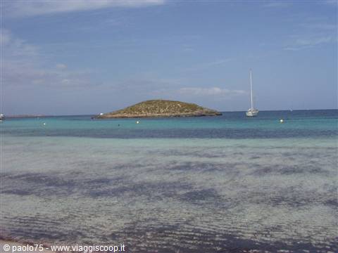 Turquoise water with seaweed, green islet and anchored sailboat