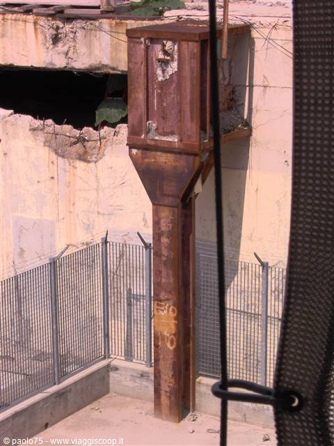 Rusty steel pillar against cracked concrete wall and wire fence in abandoned area