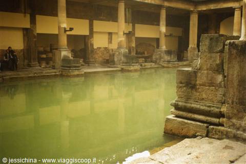 Green water of the Roman Baths in Bath among stone columns and steam