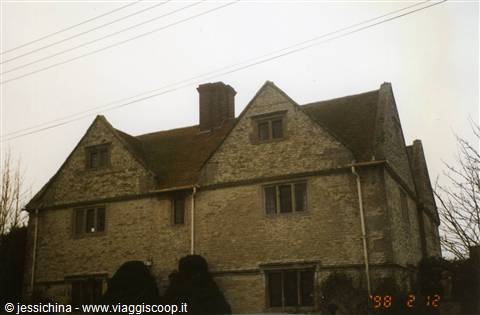 Old grey stone manor house with tiled roof and chimney under an overcast sky