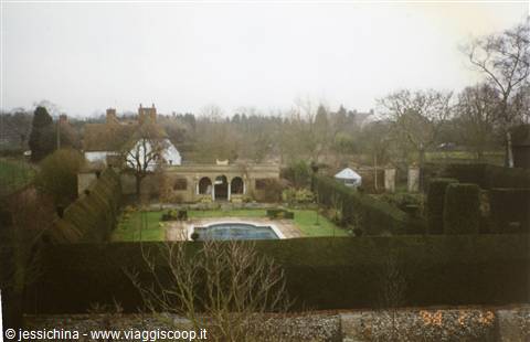 Formal garden with rectangular pool, tall hedges and English manor house behind