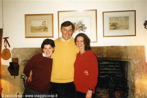 Three people hugging by the stone fireplace, framed paintings on the wall