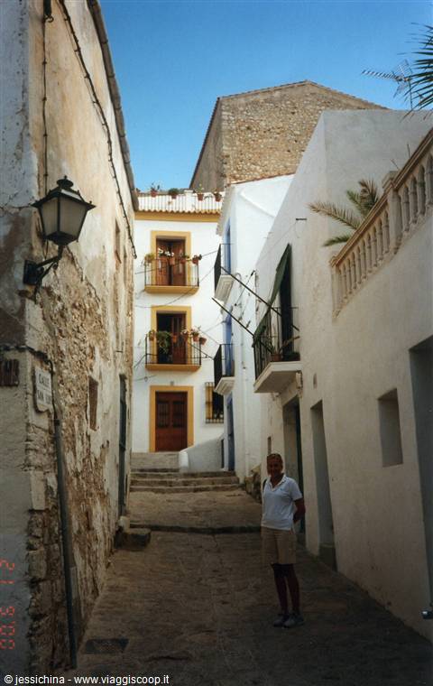 Whitewashed house with flowered balconies and stone steps, woman on the alley