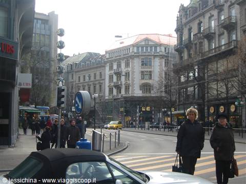 Pedestrians cross a Zurich intersection among historic buildings, UBS sign and tram