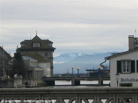 Stone bridge over the Limmat river, historic building and snowy mountains in Zurich