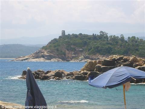 Beach umbrellas in front of rocks and an old coastal watchtower