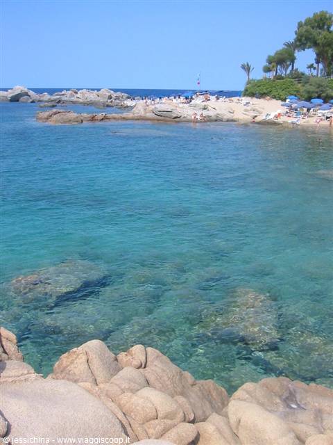 Clear turquoise water and granite rocks in front of a beach with umbrellas