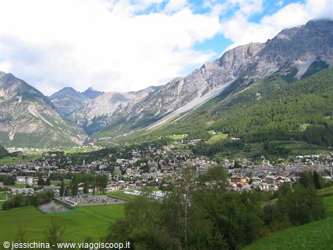 Bormio, houses beneath grassy mountains under white clouds