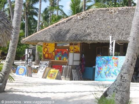 Thatched-roof beach stall selling colorful Caribbean paintings among palm trees