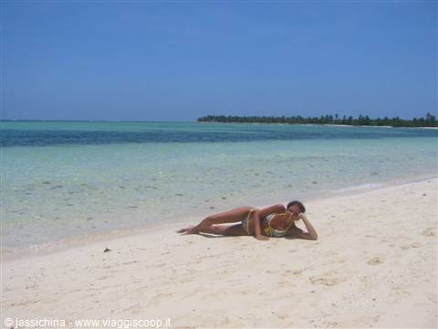 Woman in bikini lying on white sand by a turquoise sea