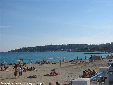 Beachgoers and umbrellas on the sand, blue sea and green hillside under clear sky