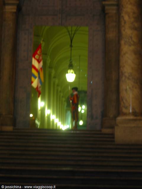 Guard with flag in lit portico at night, marble columns and stairs