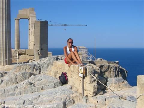 Tourist sitting on a limestone boulder among Lindos Acropolis columns, above the sea
