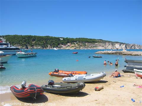 Colorful inflatable boats on beach, swimmers in turquoise water, white cliffs island