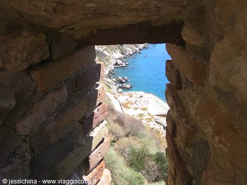 Turquoise sea among rocks seen through an ancient stone wall opening