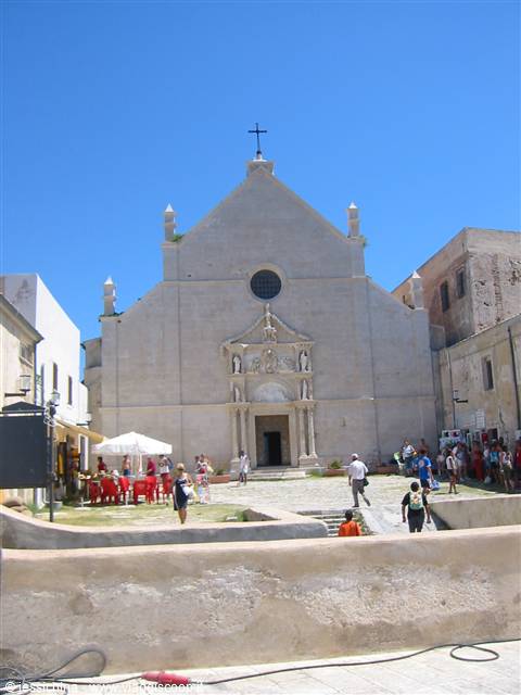 Stone cathedral facade, tourists walking in the small square under blue sky