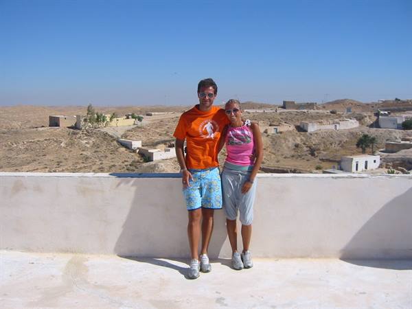 Couple on white terrace facing Berber village among arid hills under blue sky