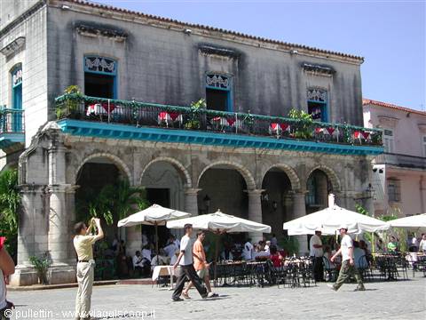 Tourists and umbrellas beneath the arcaded building of Plaza Vieja, Havana