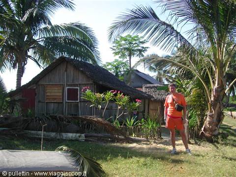 Traveler in orange standing by wooden thatched hut among palm trees and flowers