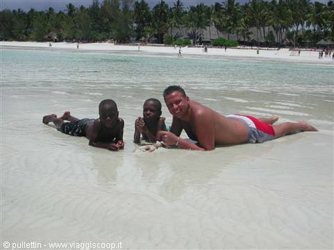 Man and two boys lying in shallow turquoise water by palm beach