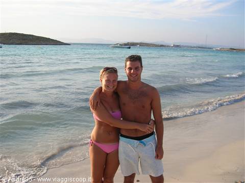 Couple in swimwear on white sand beach, turquoise sea and small islands behind