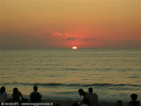 Low sun over the sea horizon, people sitting on the beach in backlight