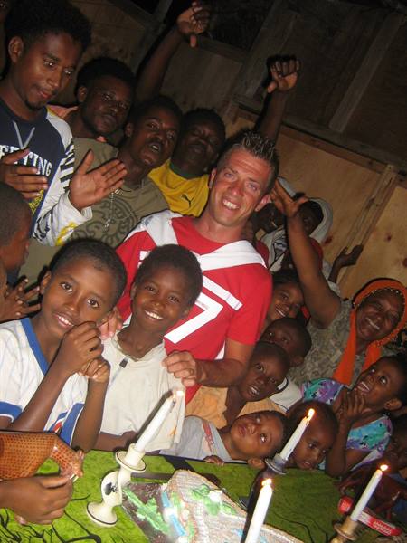 Smiling tourist in red shirt among children and lit candles in wooden house