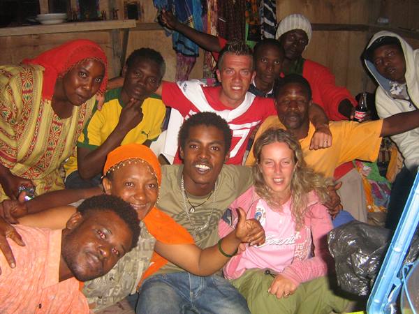 Travelers with local friends in a crowded wooden room, flash lighting